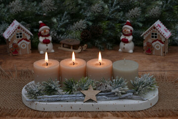 Third Advent: Natural Advent decoration with fir branches and beige candles in front of a Christmas background with space for text.