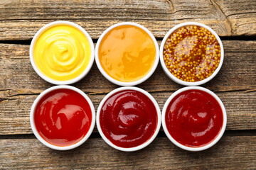 Different sauces in bowls on wooden table, flat lay