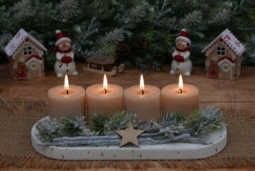 Fourth Advent: Natural Advent decoration with fir branches and beige candles in front of a Christmas background with space for text.