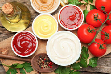 Different sauces in bowls and ingredients on wooden table, flat lay
