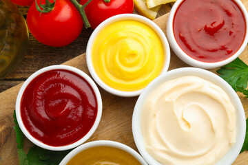 Different sauces in bowls and ingredients on wooden table, flat lay