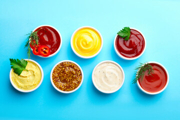 Different sauces in bowls and ingredients on light blue background, flat lay