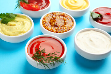 Different sauces in bowls and herbs on light blue table, closeup