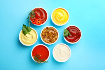 Different sauces in bowls and ingredients on light blue background, flat lay