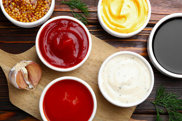Different sauces in bowls and ingredients on wooden table, flat lay