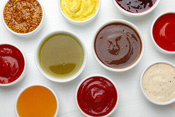 Different sauces in bowls on white wooden table, flat lay