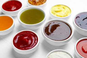 Different sauces in bowls on white wooden table, closeup