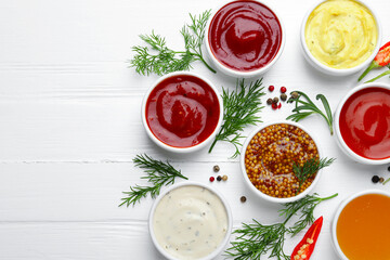 Different sauces in bowls and ingredients on white wooden table, flat lay. Space for text