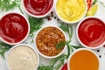 Different sauces in bowls and ingredients on white wooden table, flat lay