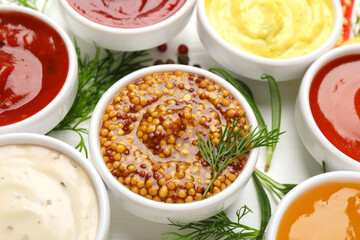 Different sauces in bowls and herbs on white table, closeup