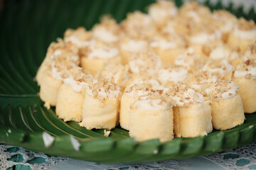 Mini sponge cakes with cream and chopped nuts on leaf platter — dessert table close-up, landscape orientation