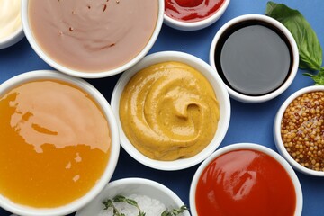 Different sauces in bowls on blue background, flat lay