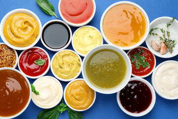 Different sauces and herbs on blue background, flat lay