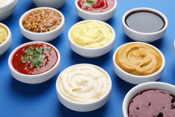Different sauces and herbs on blue background, closeup