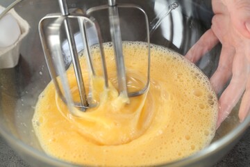 Woman beating eggs with mixer at grey table, closeup