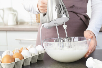 Woman beating egg whites with mixer at grey table in kitchen, closeup