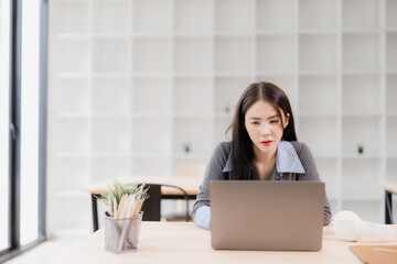 Obraz premium Asian businesswoman focusing intently on her laptop computer, working or studying at a wooden desk in a bright, modern office with a minimalist design and natural light