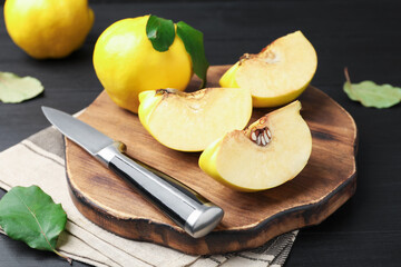 Ripe quinces, knife and green leaves on black wooden table, closeup
