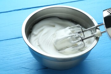 Whipped egg whites in bowl and mixer on blue wooden table, closeup