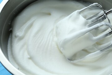 Whipped egg whites in bowl and mixer on blue table, closeup