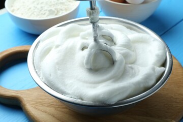 Whipped egg whites in bowl and mixer on blue wooden table, closeup