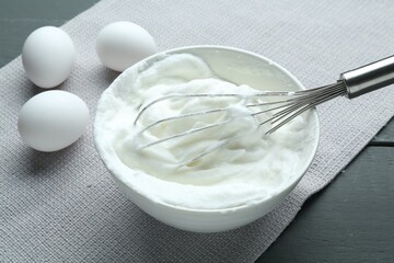 Whipped whites in bowl, whisk and eggs on grey wooden table, closeup