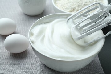 Whipped whites in bowl, mixer, flour and eggs on grey table, closeup