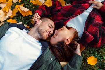Multicultural couple lying on autumn leaves smiling and cuddling outdoors.