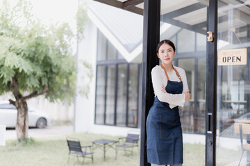 Woman small business owner stands confidently with arms crossed at her cafe entrance, smiling in apron beside an open sign welcoming customers to her new coffee shop