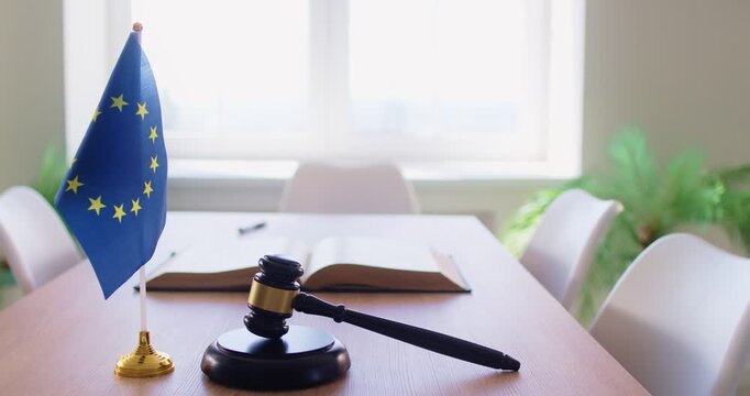 Wooden judge gavel and miniature European Union flag placed on table in conference room with no people. Concept of courtroom, law, justice, legal authority, international policy and legislation in EU.
