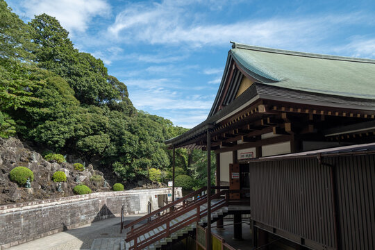 View of a traditional Japanese temple structure with a green roof nestled amongst lush greenery under a partly cloudy sky, Narita, Chiba, Japan.