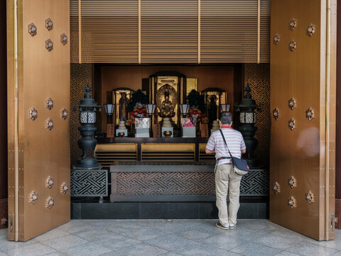 View of a man standing in front of a golden temple with intricate carvings, offering a prayer in a serene atmosphere, Narita, Chiba, Japan.
