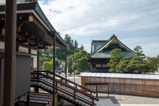 View of traditional Japanese architecture featuring dark wood, intricate roofs, and lush greenery under a cloudy sky, creating a serene atmosphere, Narita, Chiba, Japan.