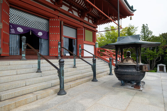 View of a traditional Japanese temple with vibrant red accents contrasting against the serene grey stone steps and lush greenery, Narita, Chiba, Japan.