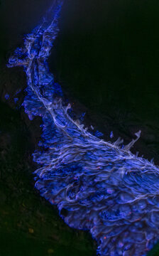 View of electrifying blue river carving through the dark landscape, its luminous glow contrasting with the inky shadows, Banyuwangi, East Java, Indonesia.