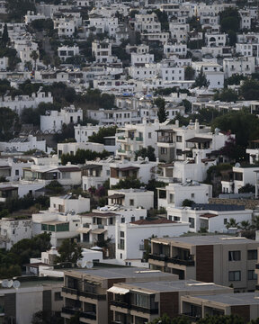 View of white buildings cascading down a hillside, a bright, dense village under a soft sky, creating a textured, architectural tapestry, Bodrum, Mugla, Turkey.