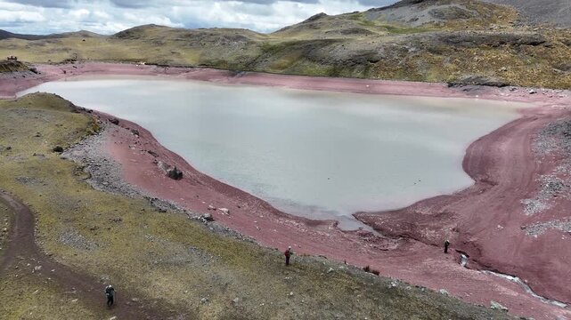 Aerial approaches Puca Cocha (Red Lake) from distance, part of the Seven Lagoons of Ausangate. Camera pans down to reveal grey waters with birds swimming in this high-altitude lake