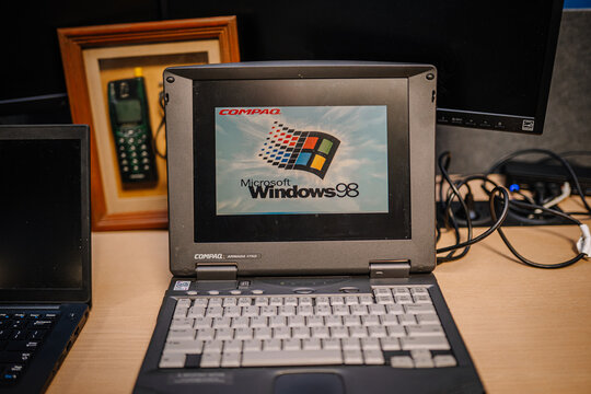 Riga, Latvia - October 24, 2025: Compaq laptop displaying Microsoft Windows 98 on a desk with vintage phone and framed photo in the background