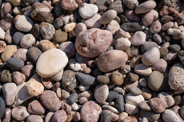 Pebbles, rocks, beach, smooth rounded stones lying on a sunny beach creating a natural texture background
