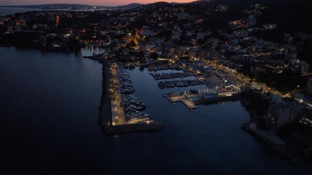 Aerial footage of yachts docking in a marina at twilight. Camera orbits Mallorca coastline, revealing luxury boats and city lights