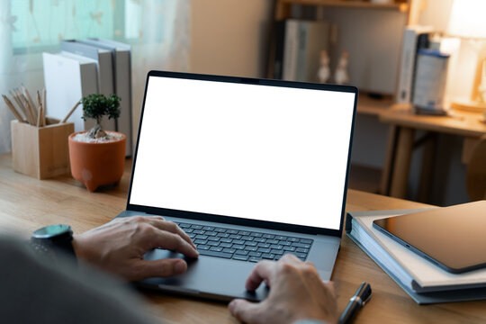Close-up of a man working on a laptop with a blank white screen mockup, ideal for demonstrating websites or applications in a modern home office setting.