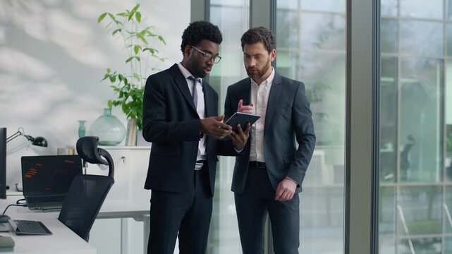 Two multiracial businessmen discussing project in modern office looking at digital tablet together multiethnic business men diverse male colleagues talking cooperation teamwork strategy planning work - Powered by Adobe