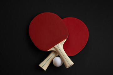 Two red table tennis paddles and a white ball arranged on a black background