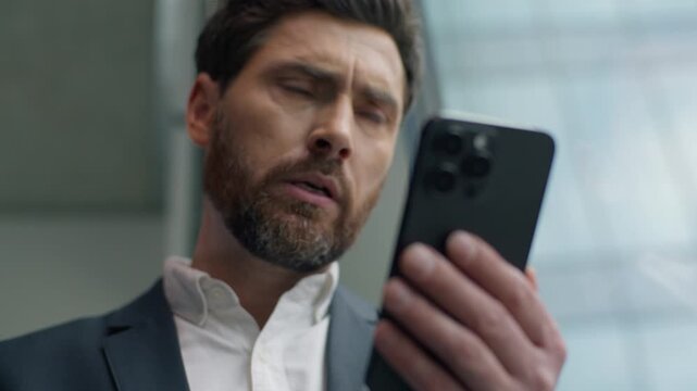 Shocked confused annoyed Caucasian male guy businessman business man in office looking smartphone reading bad news upset with mobile phone frustrated stressed failure app sad negative work problem