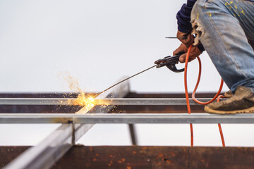 Skilled Worker Welding Metal Structure with Sparks Flying in the Air on Construction Site Amid...