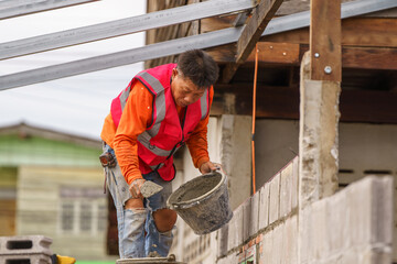 Fototapeta premium Skilled Worker in Construction Wearing Safety Vest Applying Cement on Wall at Building Site with Focused Expression and Construction Materials Around