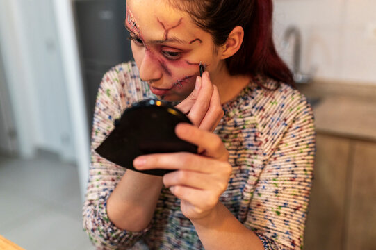 Creative teen fixing Halloween makeup details in cozy home