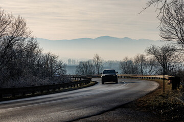 Fototapeta premium Car driving on curved winter road in misty mountains