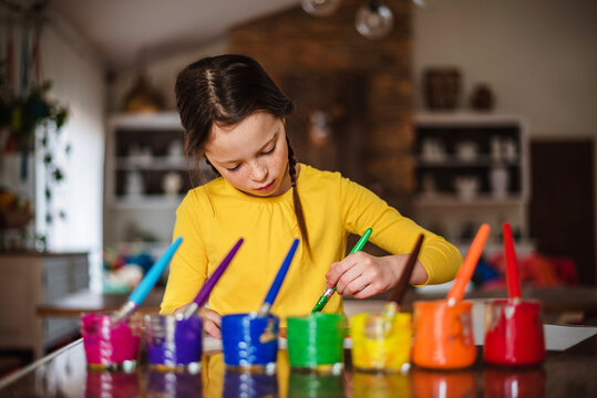 Young Girl sitting at a table in an open plan kitchen painting a picture with multi coloured paints