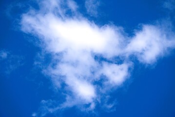 A single fluffy white cumulus cloud floating in a vibrant blue sky.